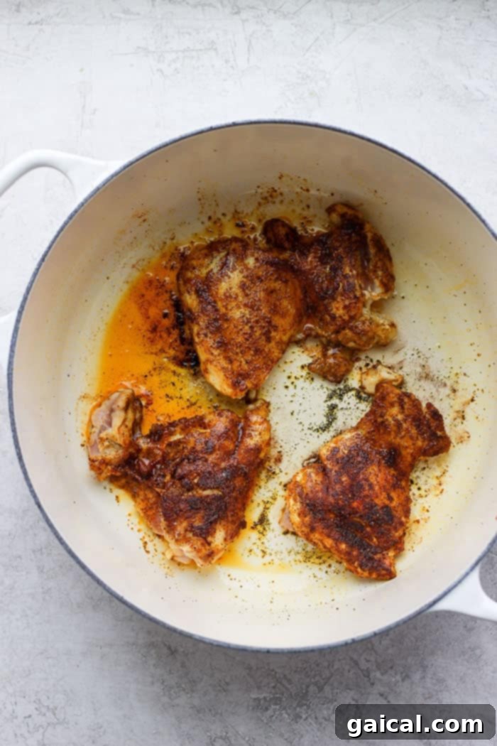 Searing Chicken Thighs for Moroccan Dish Chicken thighs being seared to a golden brown in a hot Dutch oven with olive oil.