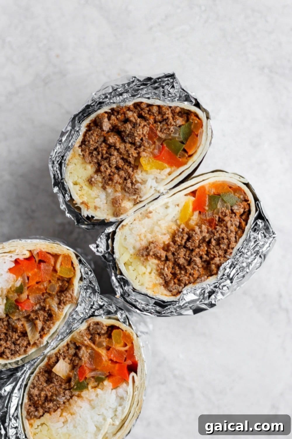 Batch Freezer Burritos 2 Two homemade frozen burritos, one unwrapped to show the delicious filling of ground beef, rice, and colorful vegetables, and another wrapped in foil for freezing.