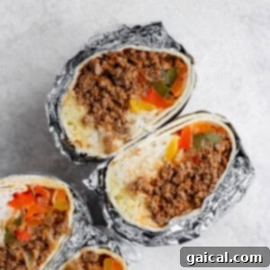 Three homemade frozen burritos wrapped in foil with meat and vegetables inside.