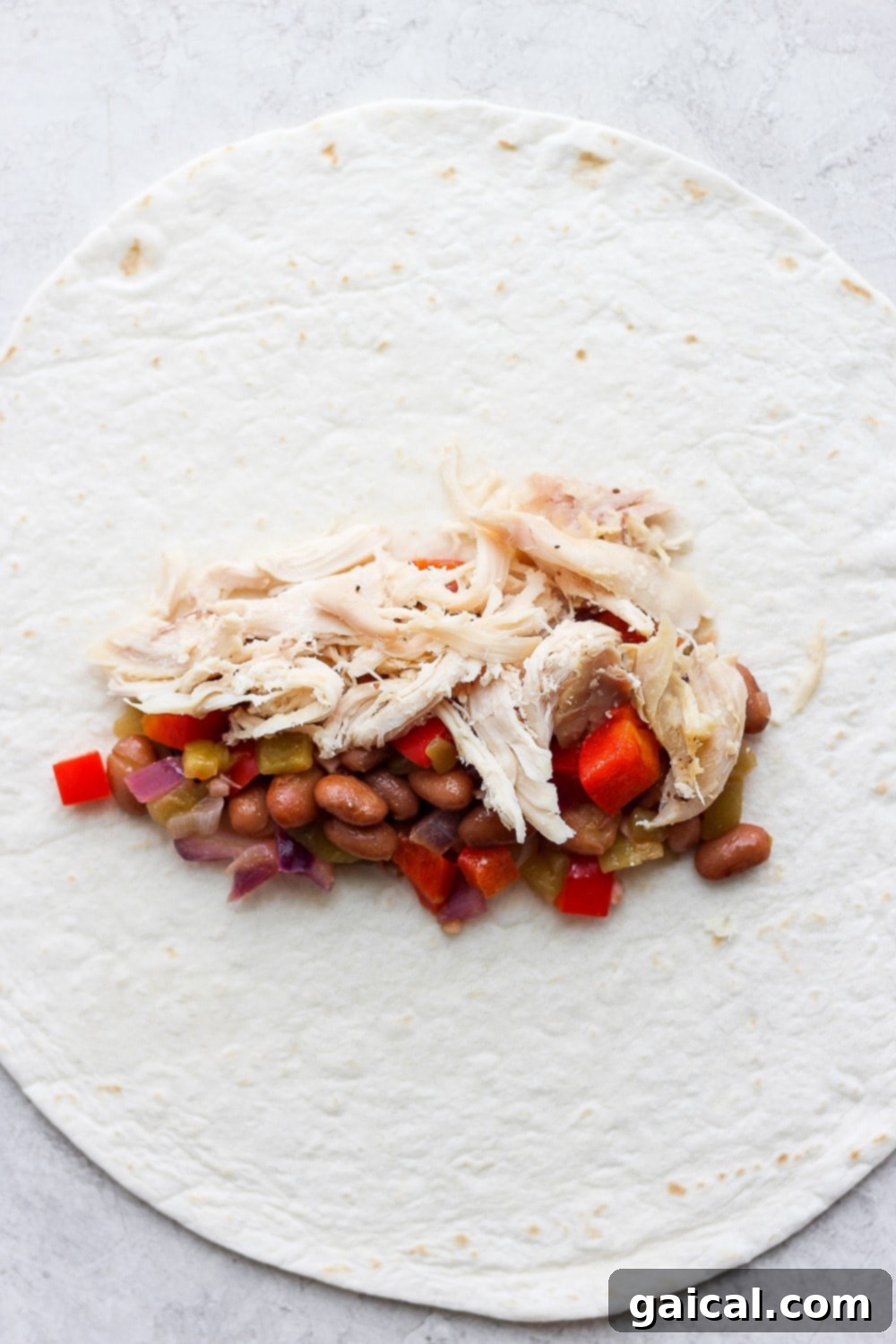 Rotisserie Chicken Enchilada Bake 4 Hands rolling a flour tortilla filled with shredded chicken and a vibrant vegetable and bean mixture for enchiladas.