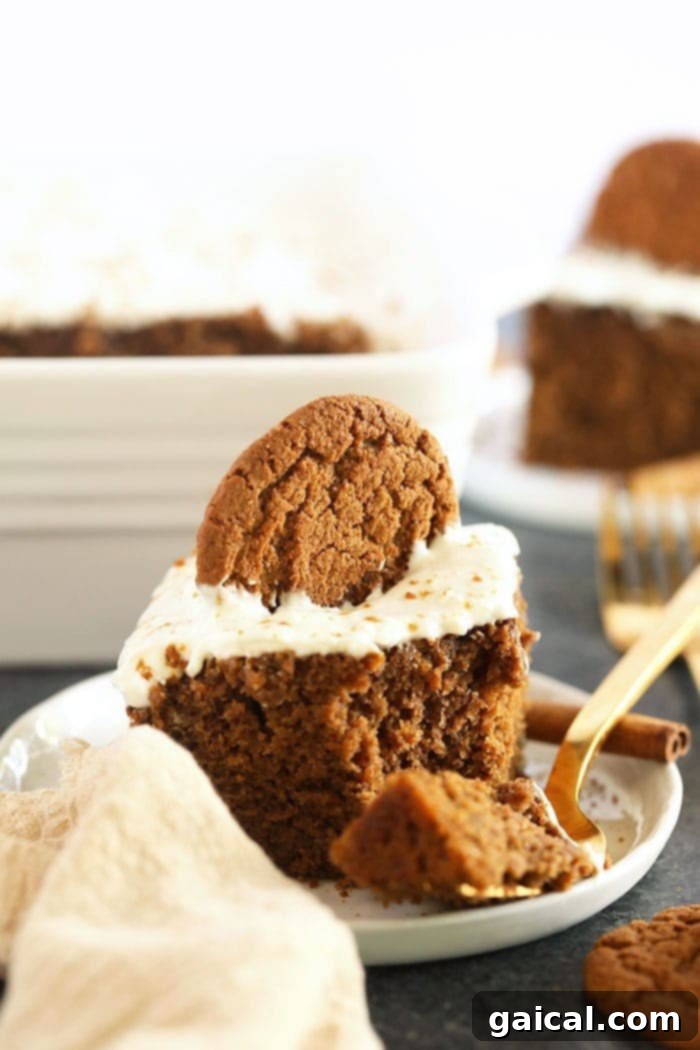 The Ultimate Classic Gingerbread Loaf with Cream Cheese Frosting slice of gingerbread on a plate topped with cream cheese frosting and a sprinkle of cinnamon