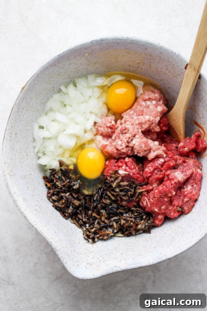 All the fresh ingredients for Wild Rice Meatloaf, including ground meats, minced vegetables, and spices, are combined in a large mixing bowl.