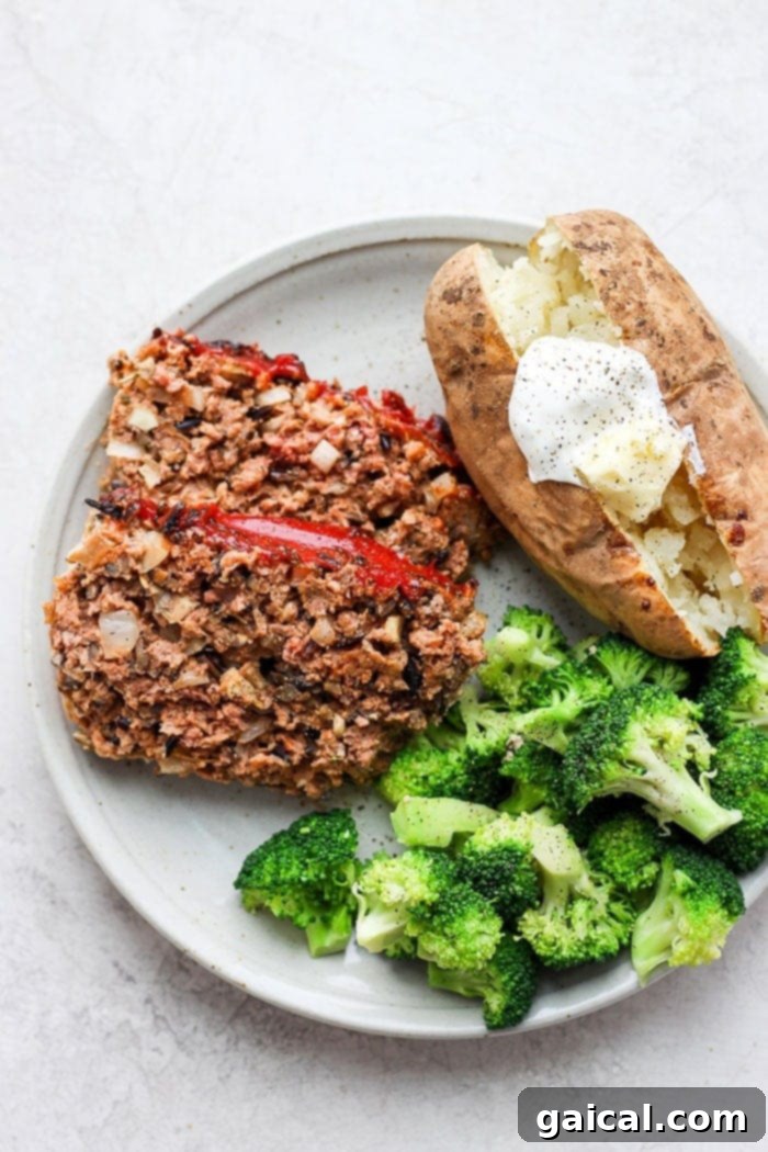 A slice of Wild Rice Meatloaf served on a white plate, accompanied by a fluffy baked potato and vibrant green broccoli florets.