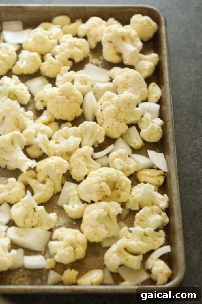 Make these cauliflower mashed potatoes for your next dinner party! They make a great low carb side dish for the holidays! Not only are they healthy, but they are insanely delicious! Cauliflower florets, onion, and garlic spread on a baking sheet, ready for roasting.