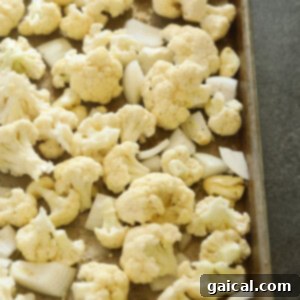 Velvety Cauliflower Mash 3 Cauliflower florets, onion, and garlic on a baking sheet, seasoned and ready for roasting.