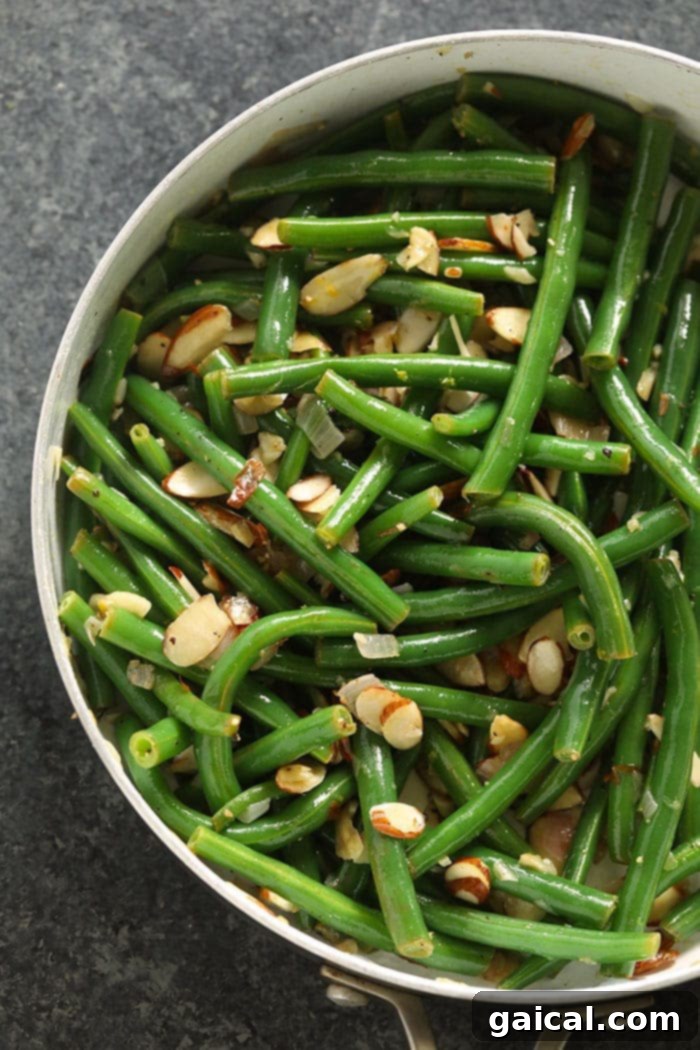 Green Beans with Toasted Almonds 4 Freshly cooked Green Beans Almondine, rich with butter and slivered almonds, ready to be served from a pan.