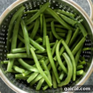 Green beans draining in a colander after being blanched and shocked in an ice bath.