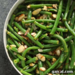 Green beans almondine being finished in a large skillet with butter, lemon, and almonds.
