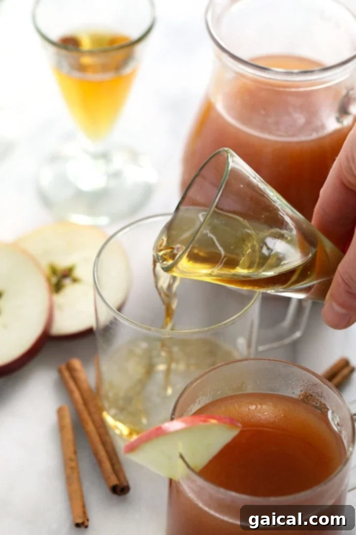 A shot of whiskey being carefully poured into a mug of warm apple cider, indicating the spiking process.
