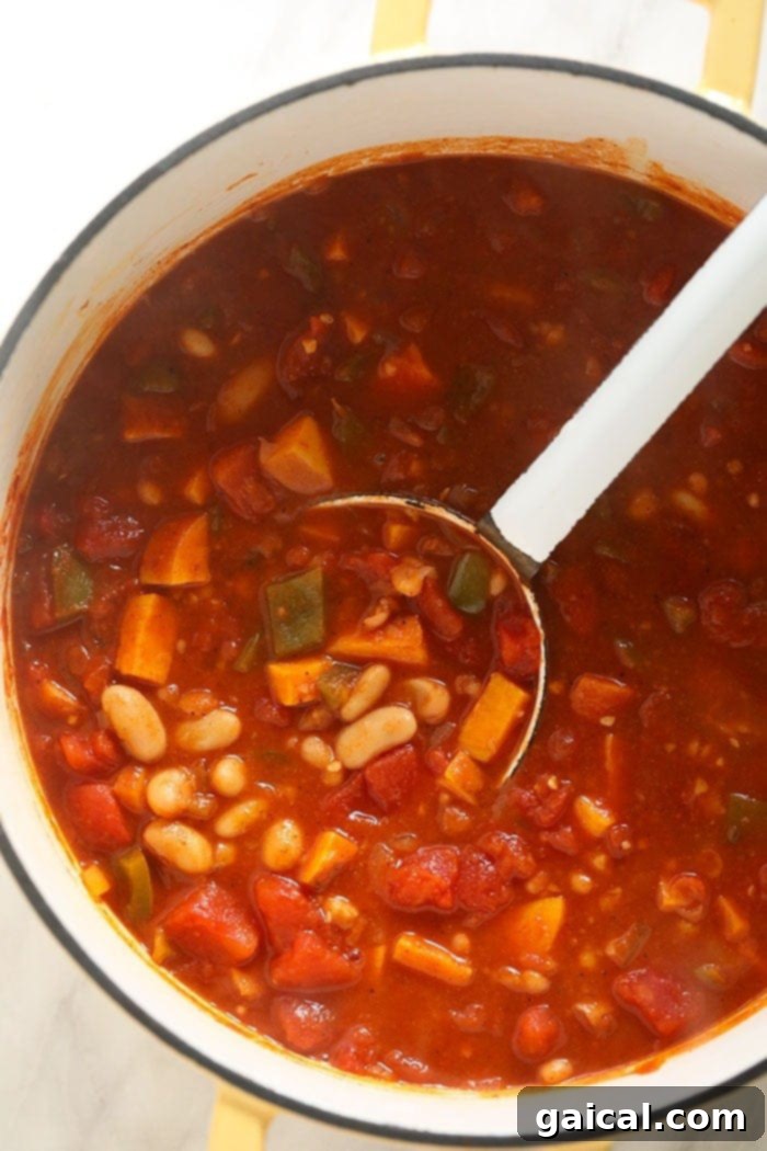 Vegetarian chili simmering in a large stockpot on the stovetop, stirred gently, with visible vegetables and beans.