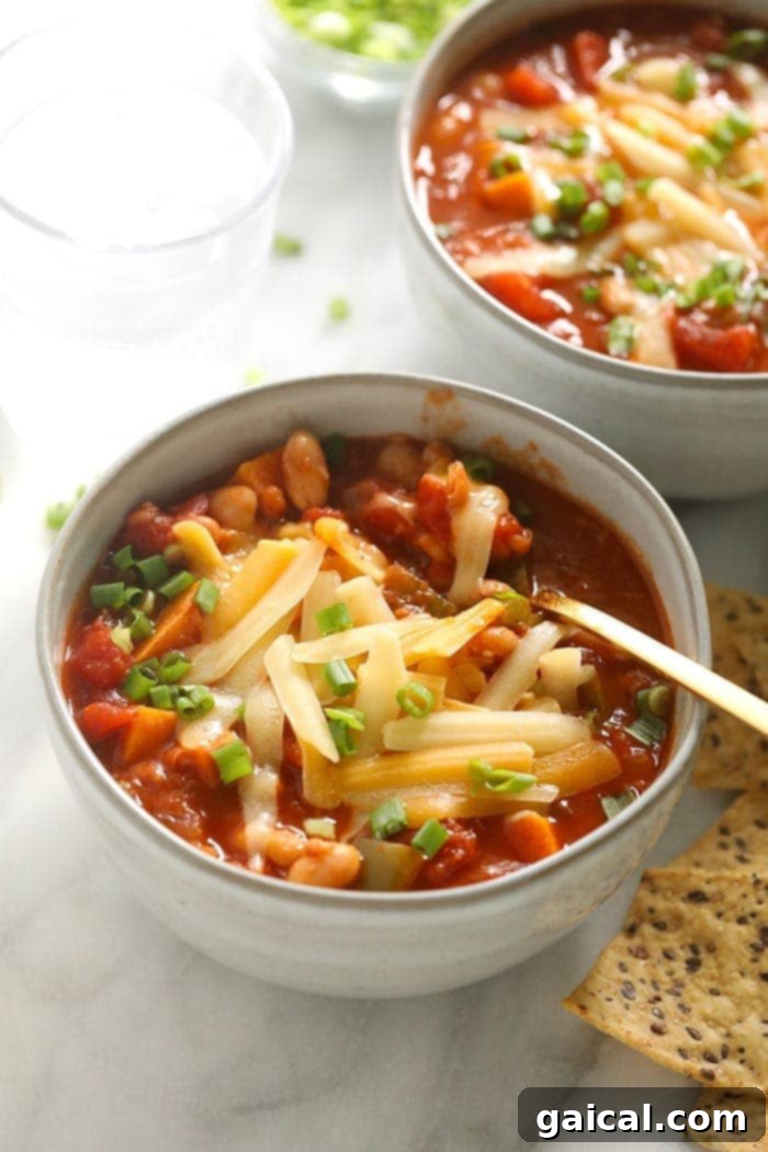 Close-up of a bowl of vegetarian chili topped with a generous amount of melted cheese and a sprig of fresh cilantro, showcasing its rich texture and inviting warmth.