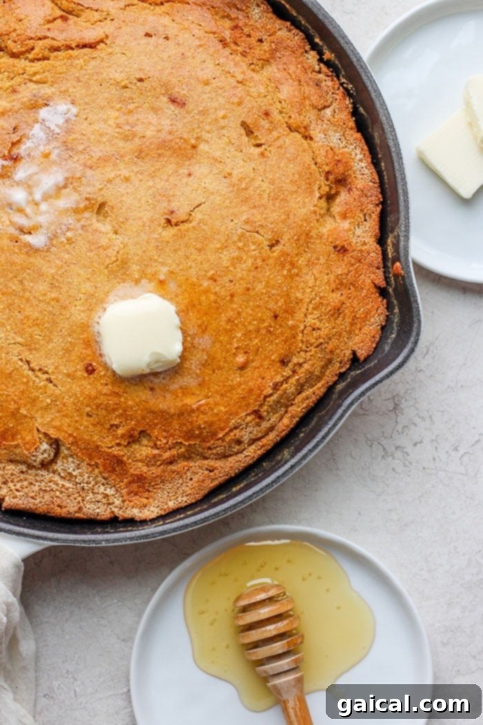 The most flavorful Healthy Cornbread with finely-ground cornmeal, white whole wheat flour, honey, and coconut oil. Melted butter spread over a slice of healthy cornbread in a cast iron skillet.