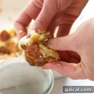A hand squeezing a roasted garlic bulb, showing the soft cloves emerging.