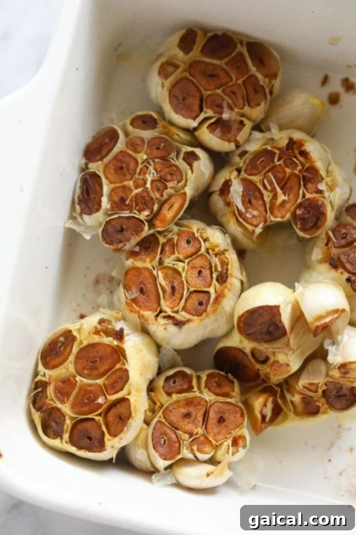 The exquisite result: beautifully roasted garlic bulbs, tender and golden. Perfectly roasted garlic bulbs with golden-brown tops resting in a baking dish.