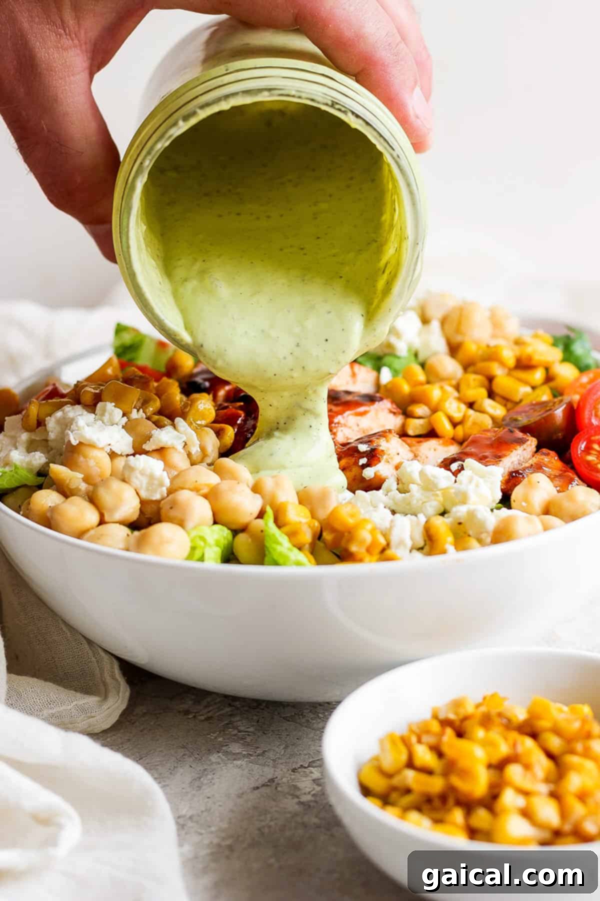 Grilled BBQ Chicken Salad 6 A hand pouring creamy green dressing over a bowl of fresh salad.