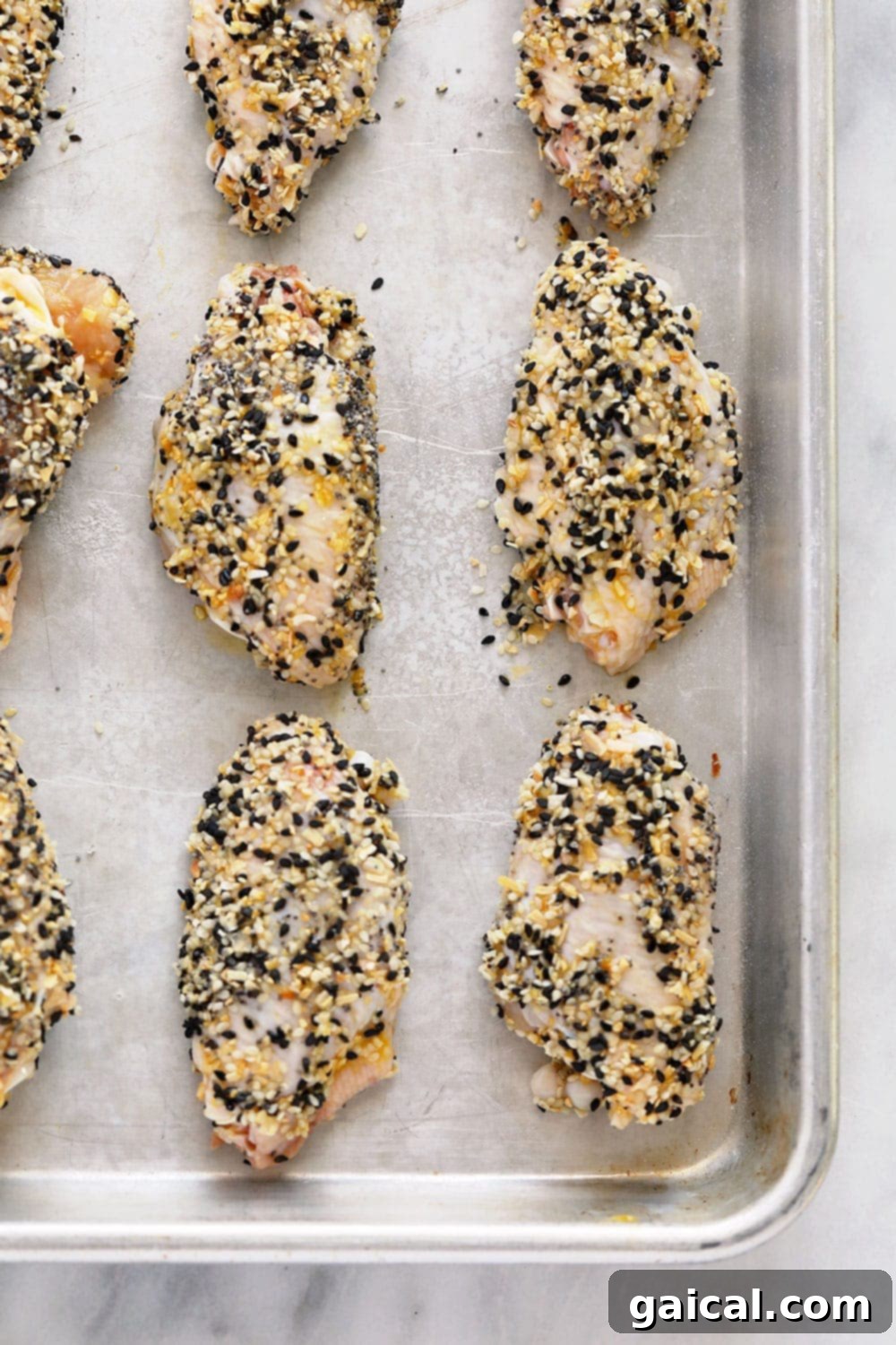 Everything Bagel Seasoning Wings on a baking sheet Uncooked chicken wings generously coated in everything bagel seasoning on a baking sheet