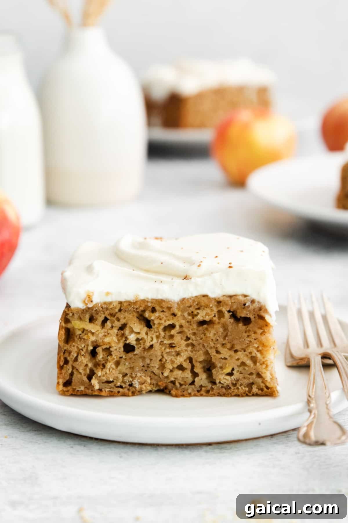 A beautifully presented slice of chai-spiced apple cake, topped with creamy white cream cheese frosting, resting on a white plate.