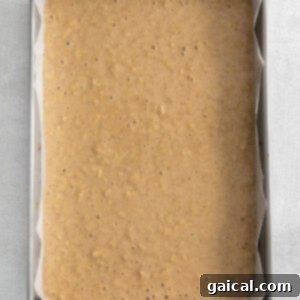 Apple cake batter settling in a parchment-lined baking pan, ready to be baked.