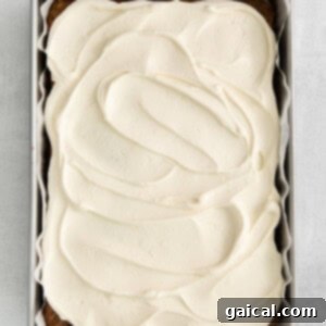 A freshly frosted apple cake with cream cheese frosting, garnished with a sprinkle of spice on top.