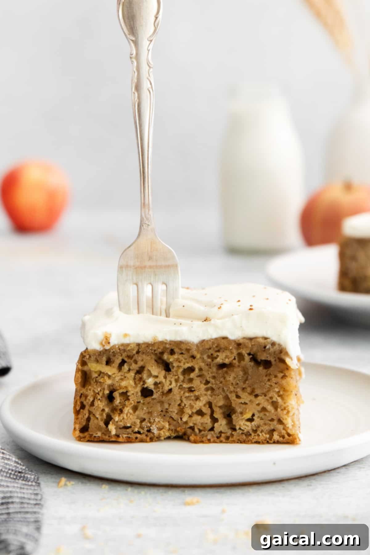 A close-up shot of a slice of apple cake with cream cheese frosting, a fork gently piercing into the moist crumb.