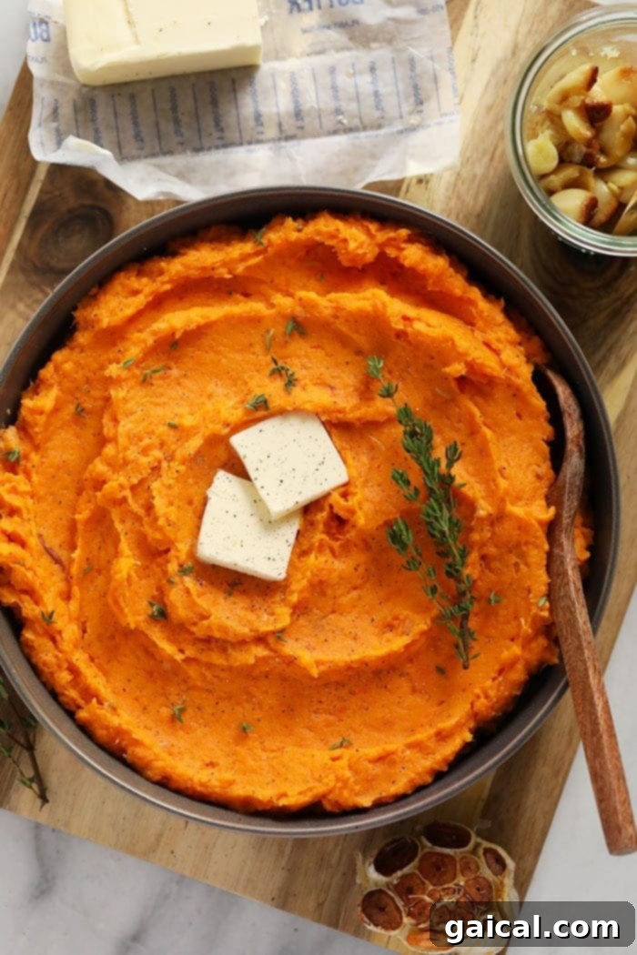 Silky smooth, buttery mashed sweet potatoes made with roasted sweet potatoes, a whole head of garlic, and a little Greek yogurt for a healthy twist. Healthy mashed sweet potatoes in a bowl with a pat of butter melting on top, garnished with fresh herbs.