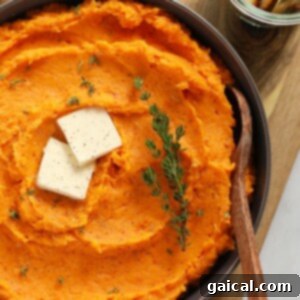 Sweet Potato Mash 6 A vibrant bowl of mashed sweet potatoes, topped with a melting pat of butter and fresh thyme, ready to be served.