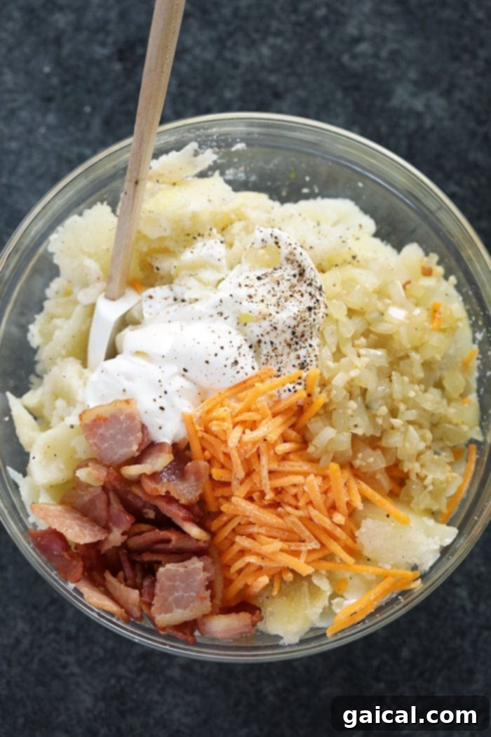 The decadent filling: a harmonious blend of creamy potato, savory bacon, and melted cheese. A rich and creamy twice baked potato filling, featuring mashed potato, bacon, cheese, and herbs, in a large mixing bowl.