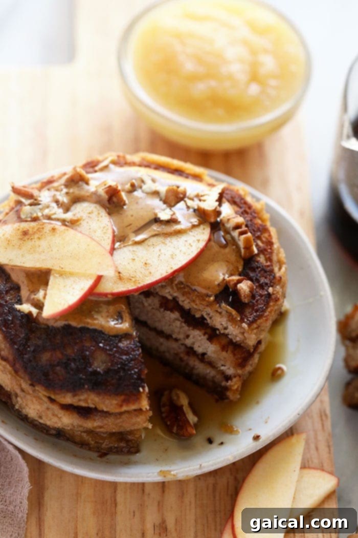 High-Protein Grain-Free Applesauce Pancakes: A Healthy & Paleo Breakfast Delight A stack of golden brown applesauce pancakes on a white plate, garnished with fresh apple slices and a drizzle of creamy nut butter, ready for a healthy and delicious breakfast.