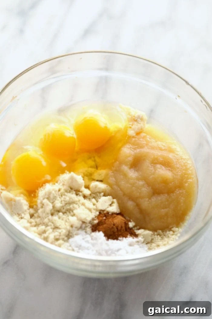 Essential Ingredients for Grain-Free Applesauce Pancakes Individual ingredients for applesauce pancakes laid out in a bowl, showcasing fresh eggs, almond flour, and unsweetened applesauce, ready for mixing.