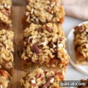 Apple crisp bars with granola and pecans, resembling apple pie bars, displayed on a cutting board, ready to be chilled and sliced.