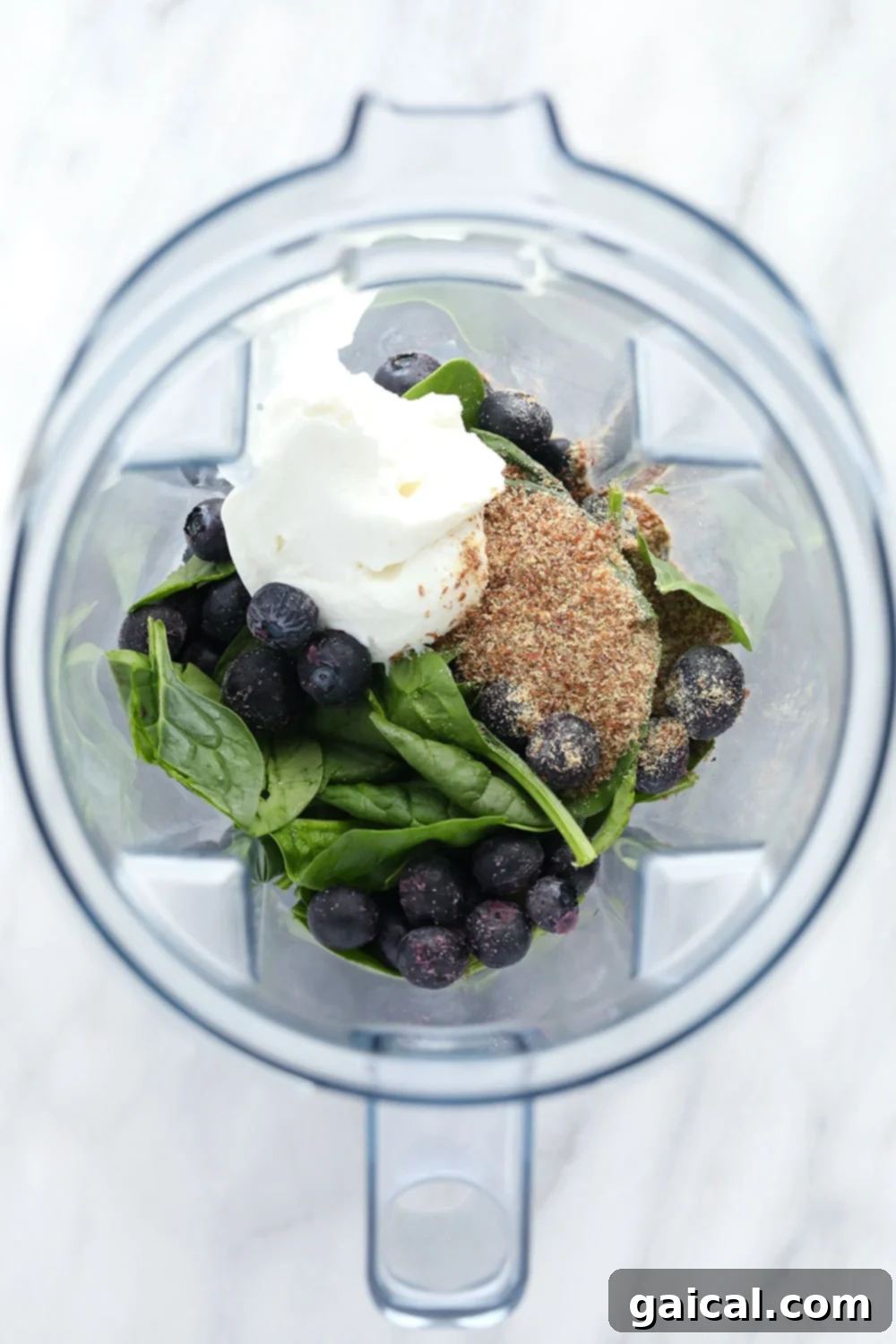 Various smoothie ingredients, including blueberries, spinach, and Greek yogurt, arranged around a blender.