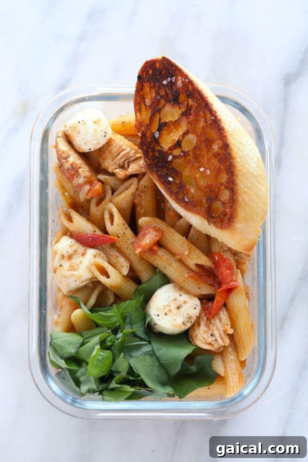Caprese Chicken Pasta with fresh ingredients in a meal prep container.