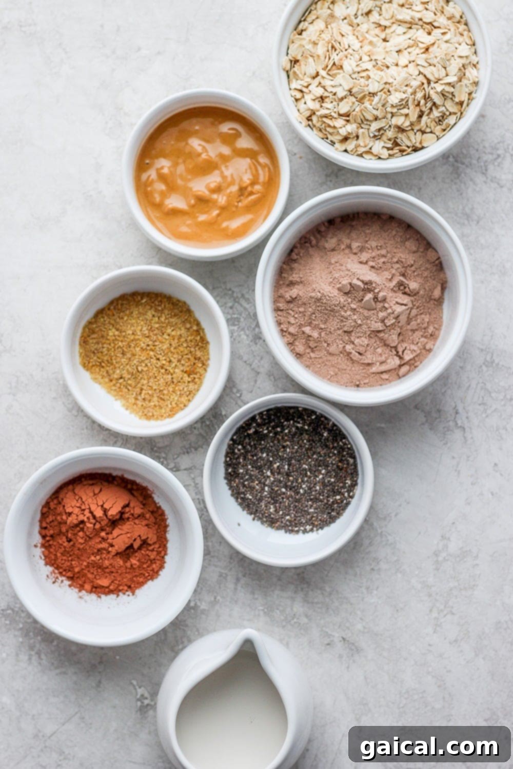 Chocolate Protein Oatmeal Ingredients Bowls of individual chocolate protein oatmeal ingredients laid out on a clean surface, ready for cooking. Includes oats, protein powder, cocoa, flaxseed, and chia seeds.