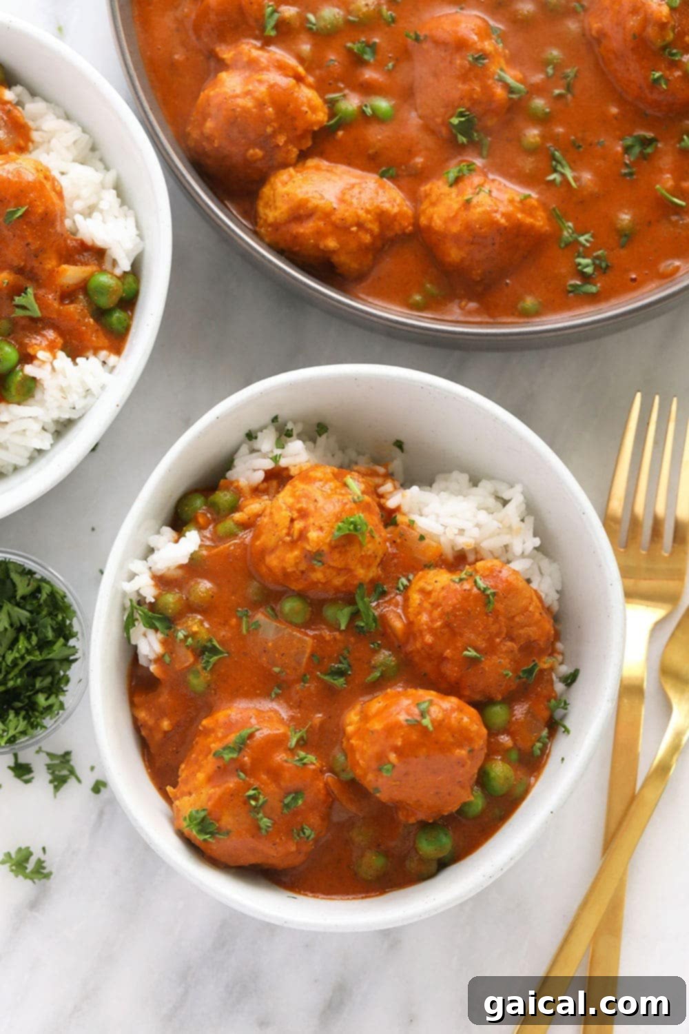 A beautifully presented bowl of Tikka Masala Meatballs, generously coated in a rich, orange-hued sauce, served alongside white rice and garnished with fresh green herbs. The meatballs are perfectly browned and inviting.