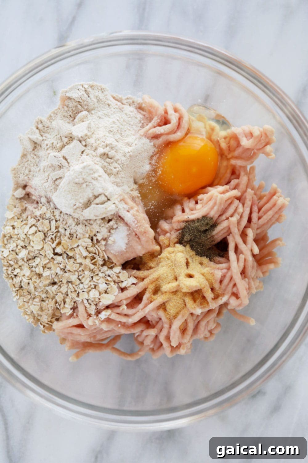 A carefully arranged flat lay of all necessary ingredients for Tikka Masala Meatballs: ground chicken, quick-cooking oats, flour, egg, spices, olive oil, onion, peas, canned coconut milk, and tomato sauce, neatly displayed in bowls.