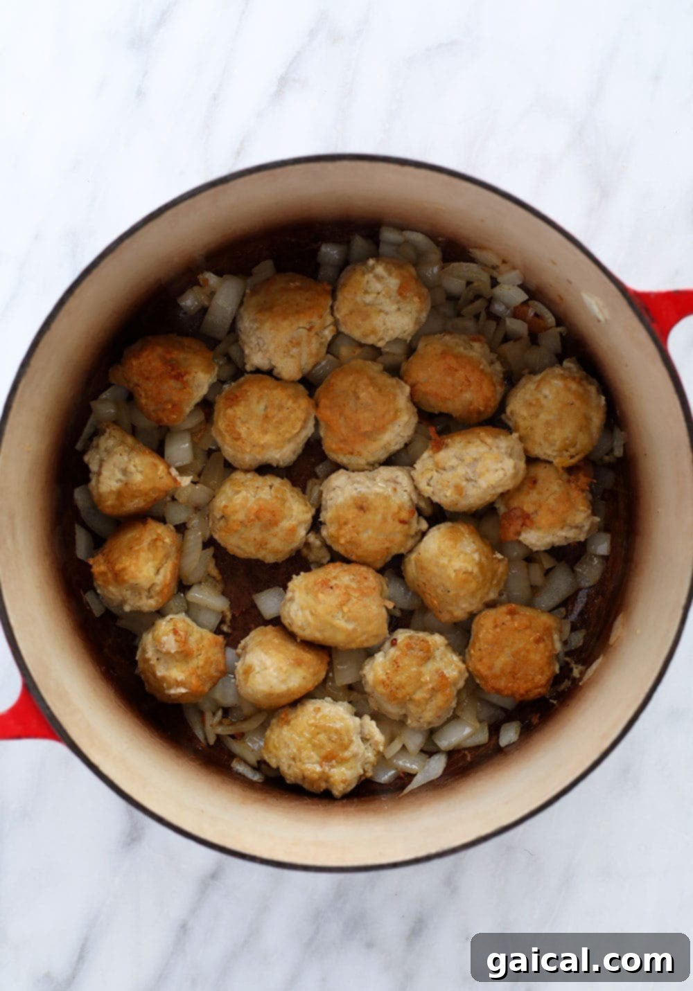 Close-up shot of ground chicken meatballs being carefully turned in a hot Dutch oven, where they are browning to a perfect golden-crisp in olive oil.