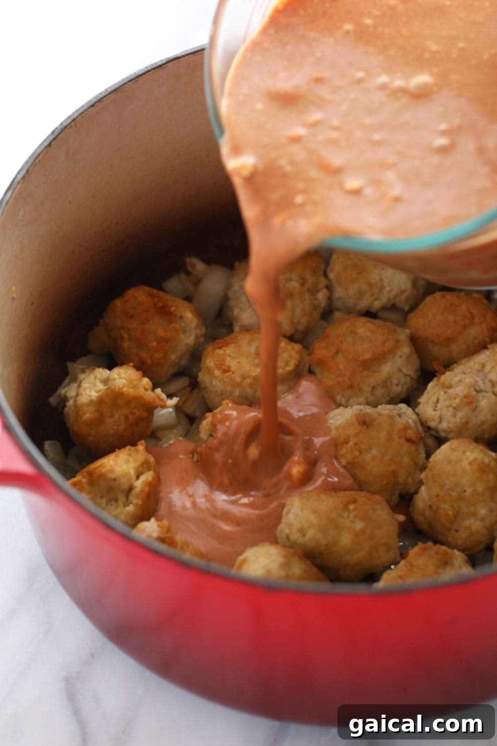 A ladle expertly pouring generous amounts of rich, orange tikka masala sauce over a bowl filled with tender chicken meatballs, highlighting the creamy texture of the sauce.