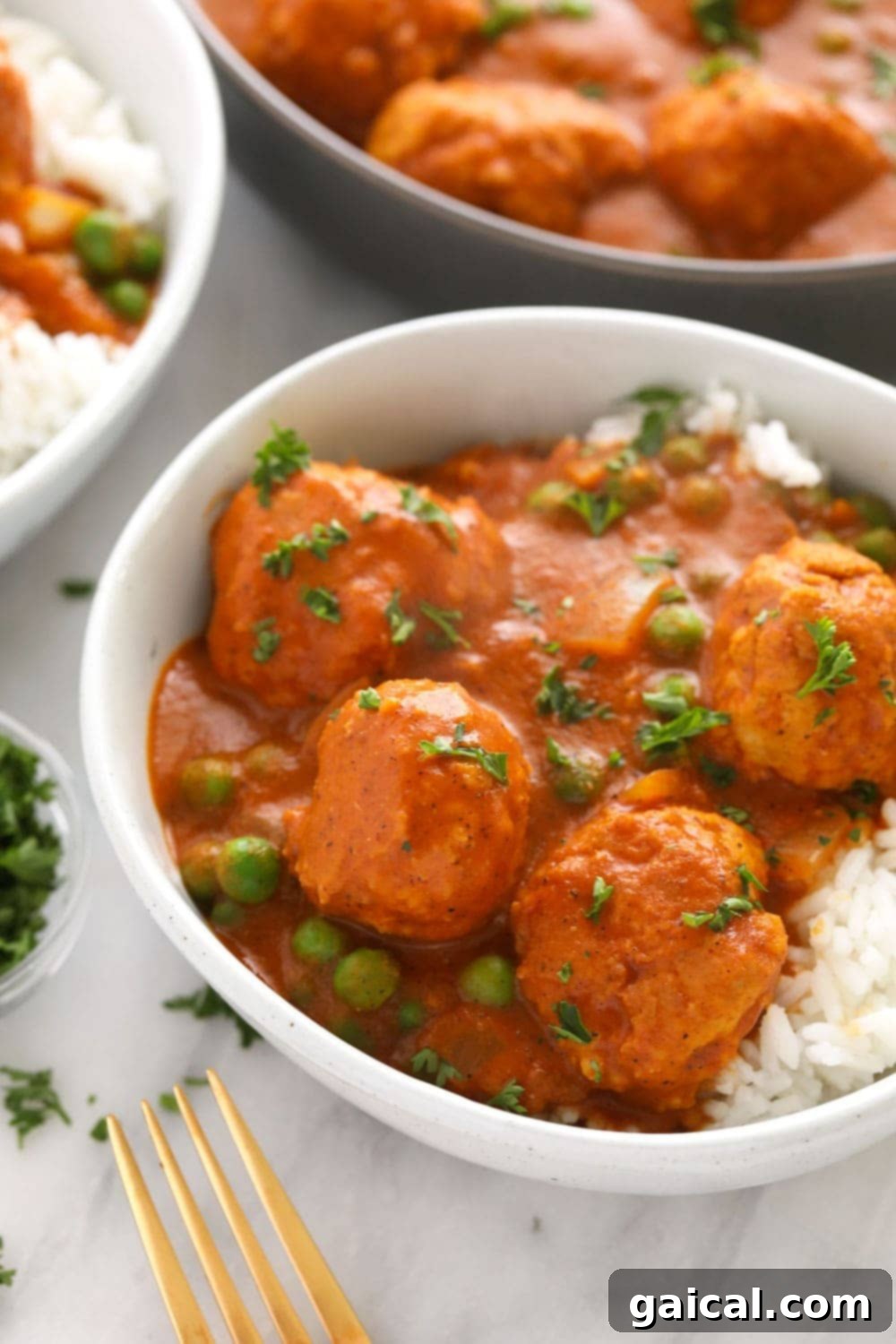 A close-up shot of Tikka Masala Meatballs served over fluffy white rice in a rustic ceramic bowl, garnished with vibrant fresh parsley, ready to be enjoyed.