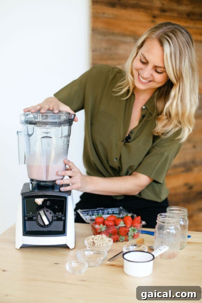 A woman smiling while operating a high-speed blender, making a protein shake in a modern kitchen.