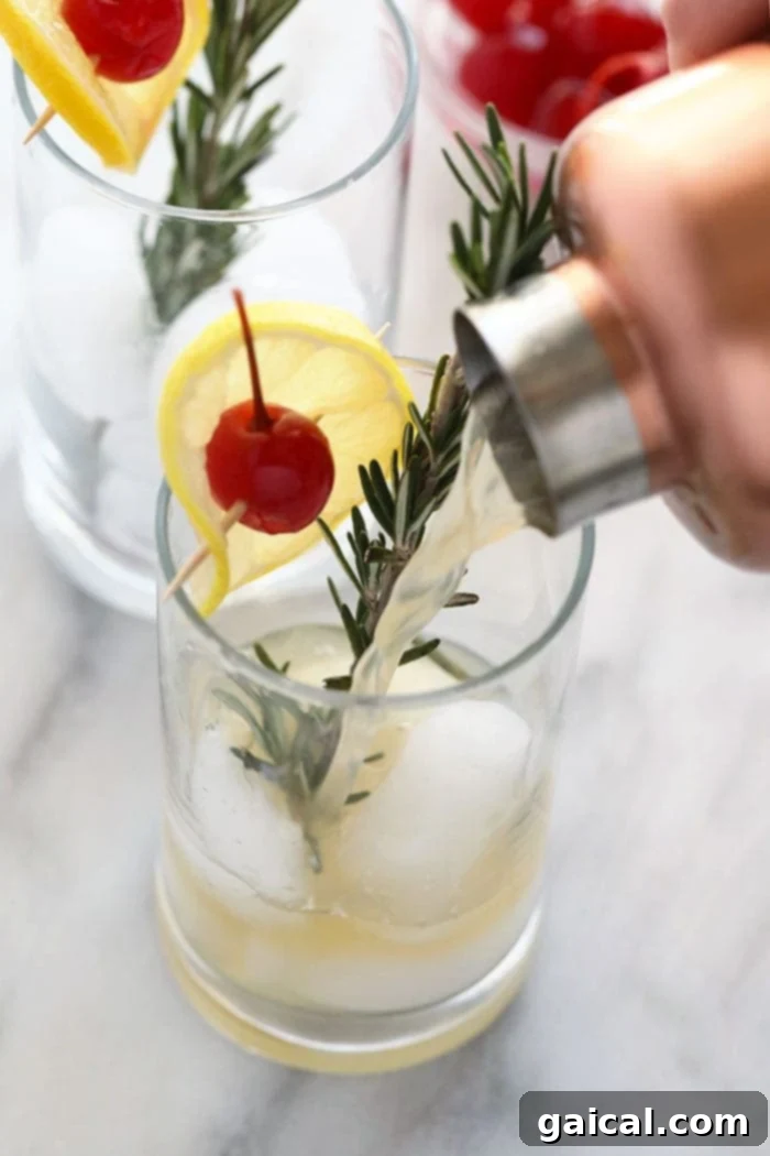 Someone pouring a Rosemary Collins cocktail into a glass filled with ice, garnished with rosemary.