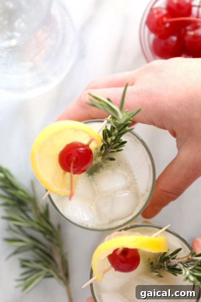 Close-up of a Rosemary Collins in a glass, garnished with a sprig of fresh rosemary, a lemon slice, and a maraschino cherry.
