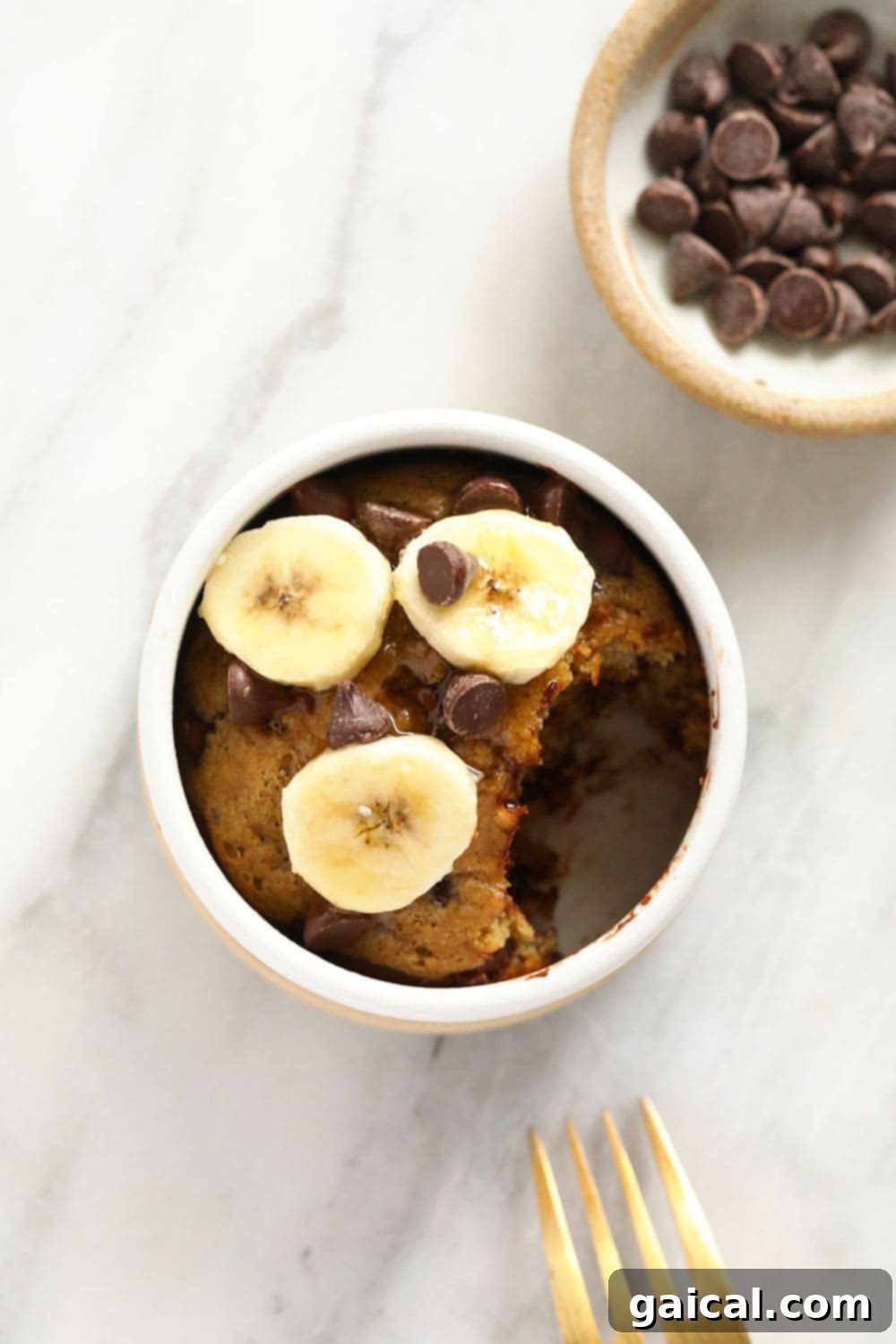 Close-up of a warm, fluffy banana mug cake in a white mug, showing its tender crumb and melted chocolate chips.