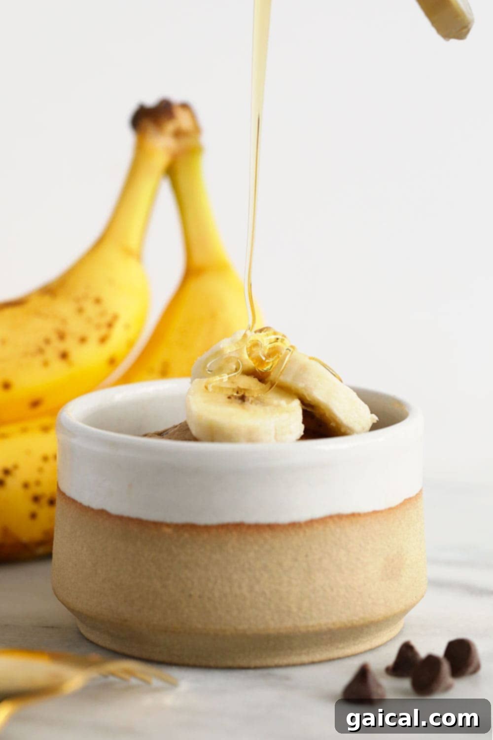 Close-up of a warm banana mug cake with melted chocolate chips and a tender, moist interior, served on a small plate next to a spoon.