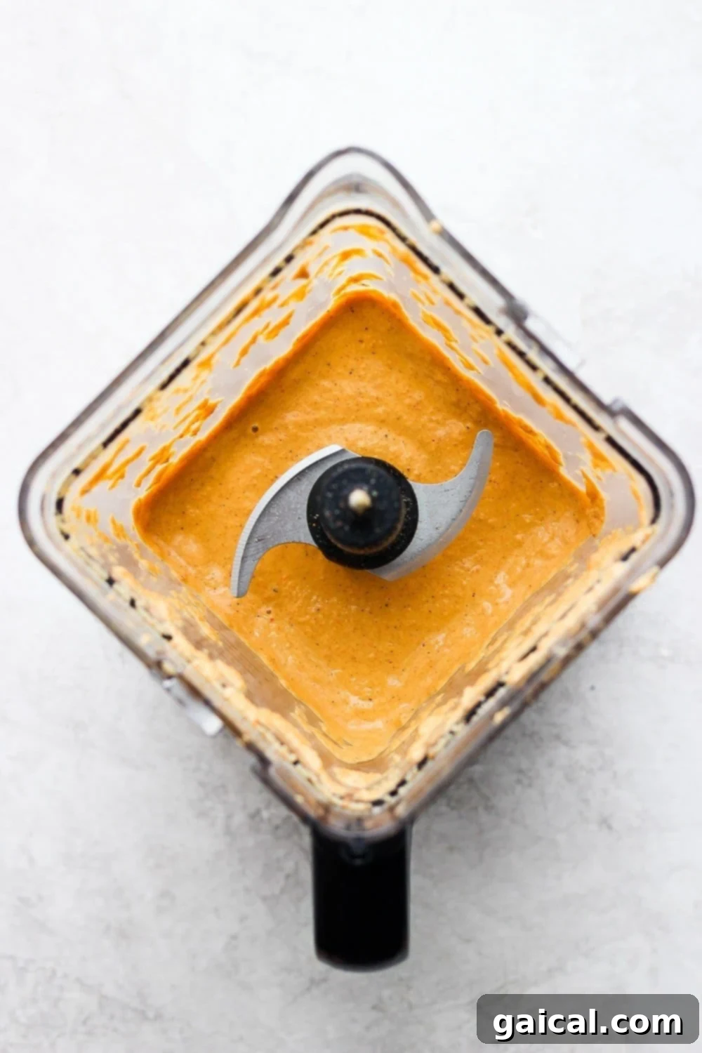 A high-speed blender processing creamy vegan queso, illustrating the smooth, rich texture of the plant-based cheese sauce.