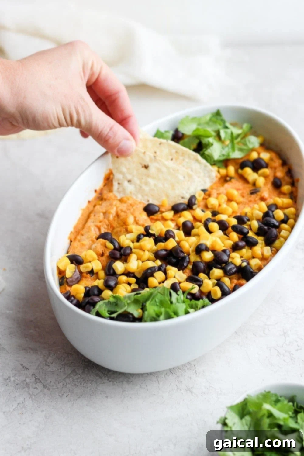 A tortilla chip being dipped into the creamy, baked Vegan Mexican Street Corn Queso Dip, showing its rich texture and enticing color.