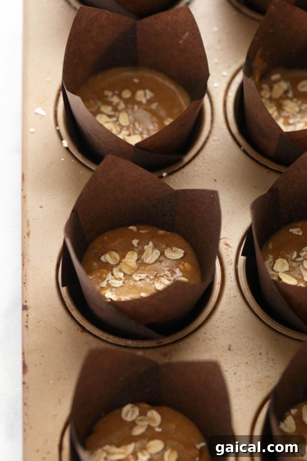 Preparing Healthy Oatmeal Muffins: A Step-by-Step Guide to Wholesome Baking Unbaked classic oatmeal muffin batter perfectly scooped into a muffin pan, generously topped with a sprinkle of rolled oats, and ready for baking.