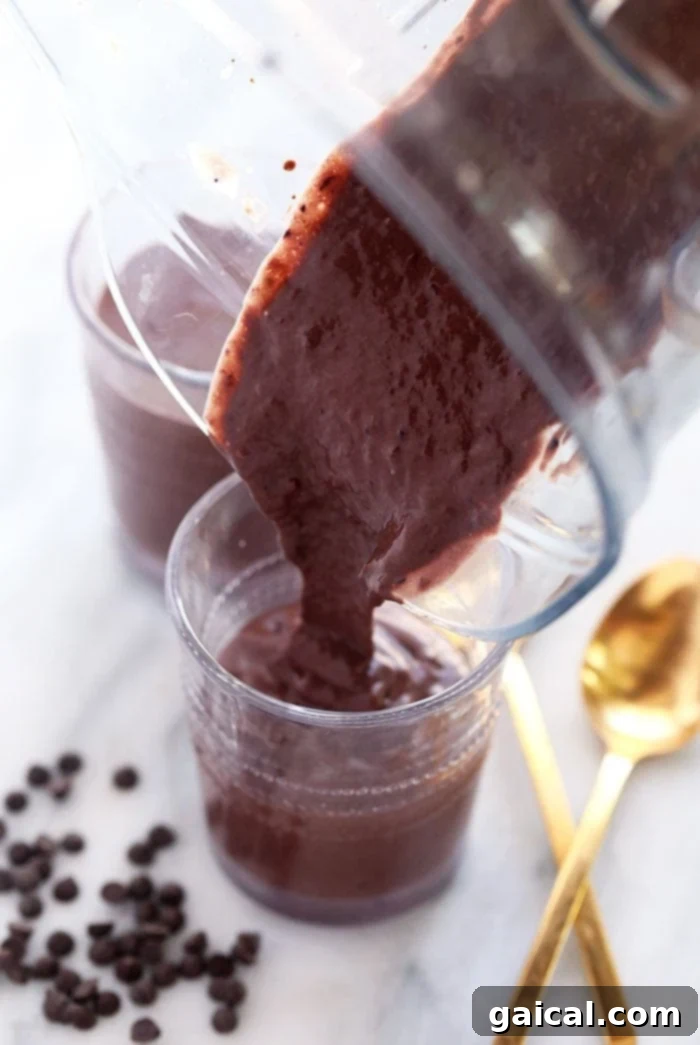 Creamy chocolate protein shake being poured from a high-speed blender into a tall glass, showcasing its incredibly smooth and thick texture.