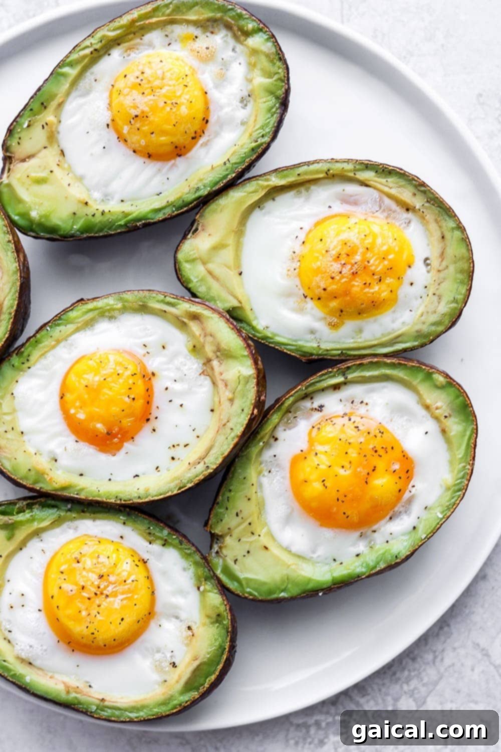 A close-up of an avocado baked egg on a plate, topped with chives and bacon bits.