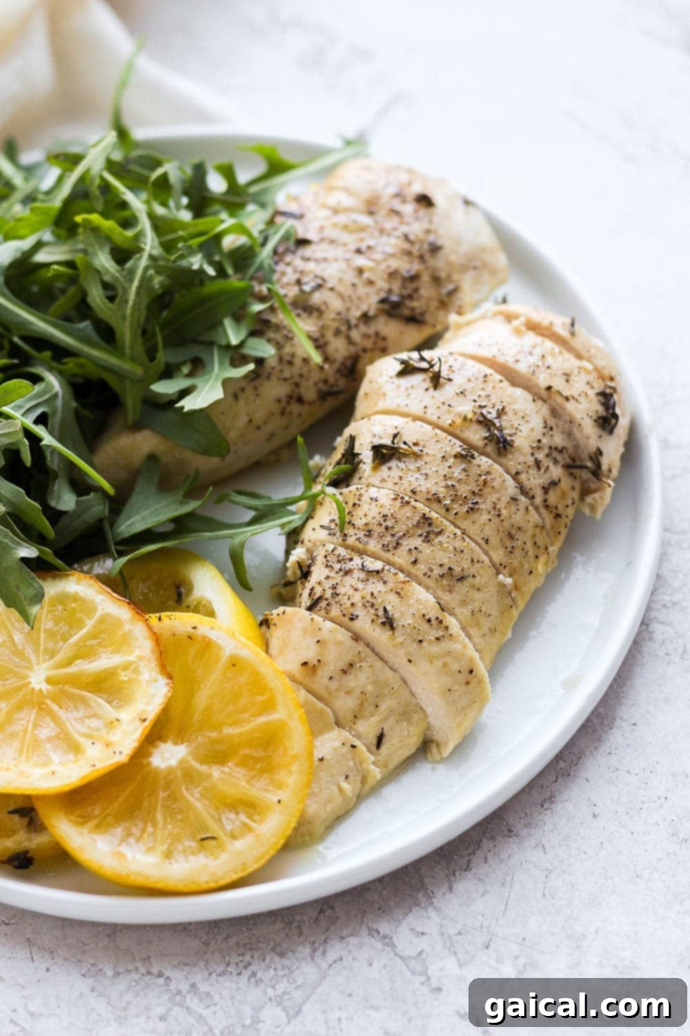 Sliced baked lemon chicken on plate, garnished with fresh herbs.