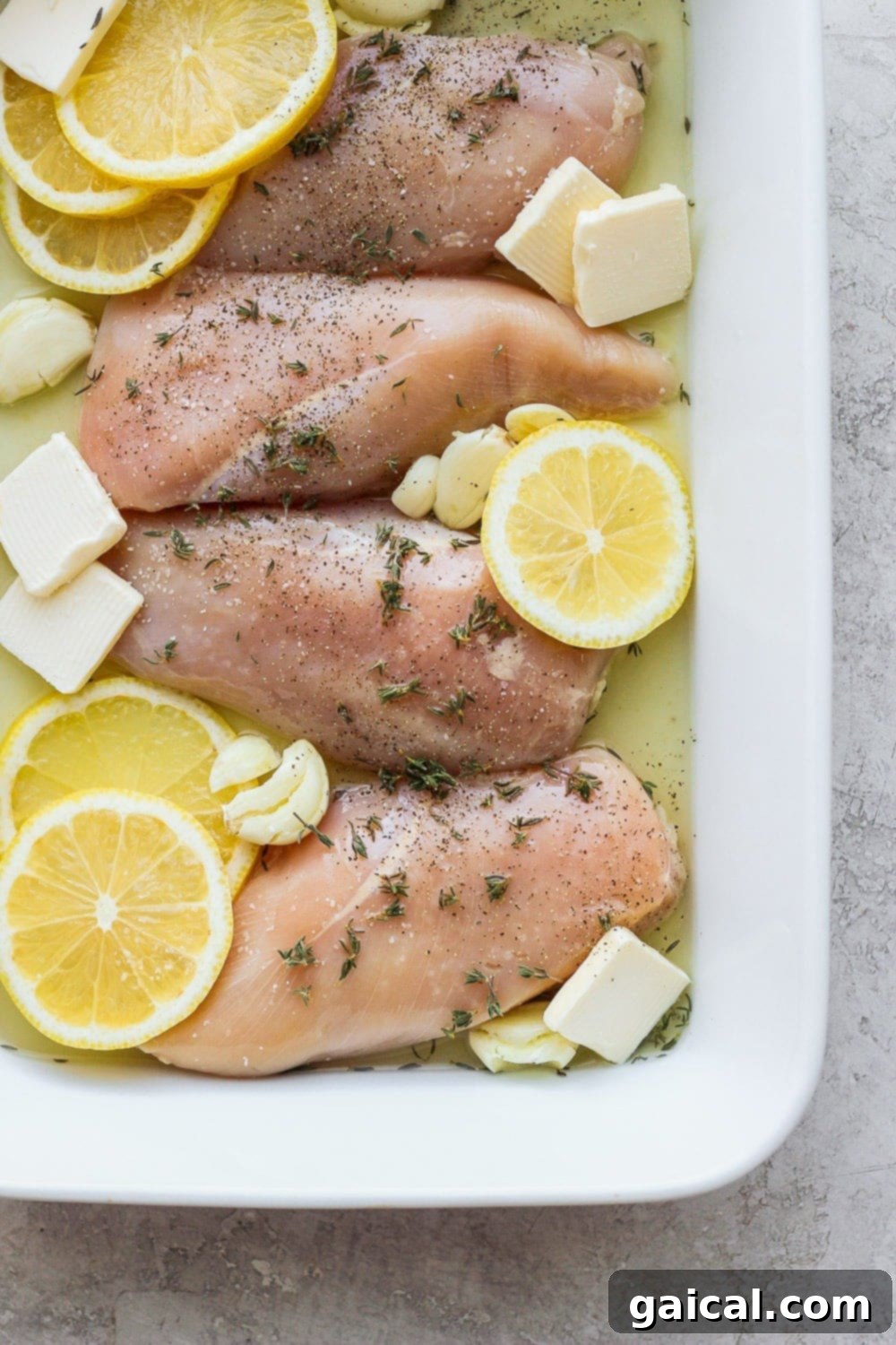 Raw chicken breasts generously seasoned with lemon, garlic, and butter, ready for baking.